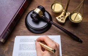 Mano firmando un documento legal con un mazo de juez y balanza de la justicia al fondo, representando Servicios Jurídicos Digitales impulsados por Inteligencia Artificial.