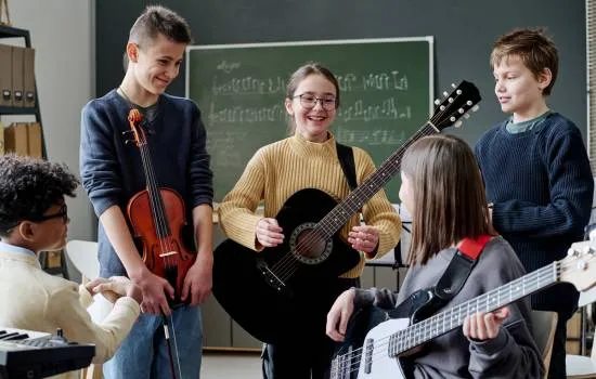 Grupo de jóvenes sonrientes tocando instrumentos musicales en un aula, representando el entusiasmo por aprender música en equipo.