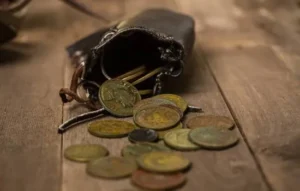 Monedas antiguas saliendo de una pequeña bolsa de cuero sobre una mesa de madera