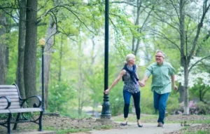 Pareja mayor caminando de la mano por un parque frondoso, disfrutando del momento mientras recuperar energía con aire puro y conexión mutua.