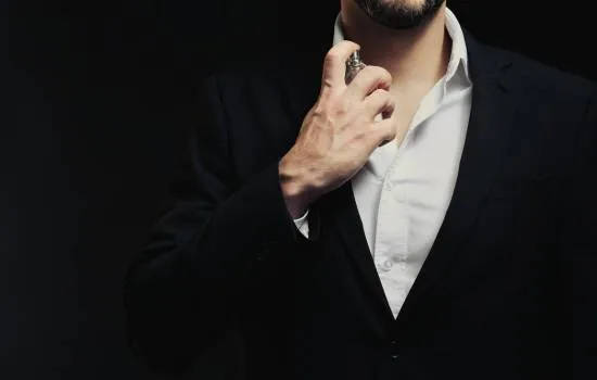 Hombre con traje elegante aplicando perfume, representando confianza y potencia masculina.